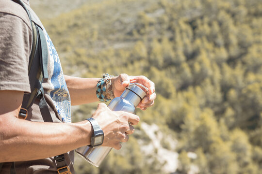 Hand taking an aluminum thermal bottle to hydrate on a hiking trail