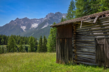 Wooden alpine hut on green meadow in front of dolomites mountains