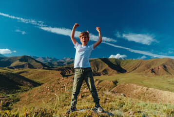 Happy boy at summer day standing in mountains in a heroic pose - 652049647