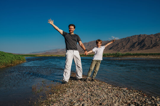 Happy father and son standing on the shore of mountain lake holding hands - Powered by Adobe