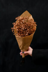 Gypsophila dried flowers bouquet of brown color wrapped in paper on dark background
