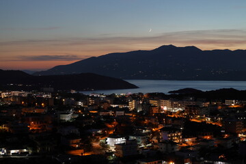 Night view of the city Ksamil in Albania on the background of Corfu island and moon. Amazing Albanian Riviera