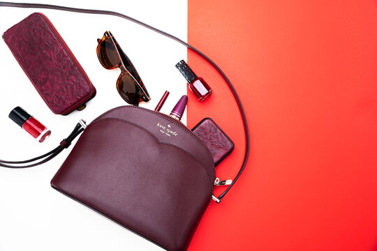 Women's handbag from Kate Spade in raspberry color and accessories on a white and red background.