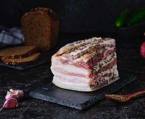 Appetizer, salted lard with streaks of meat, sprinkled with caraway seeds and garlic, on a black...
