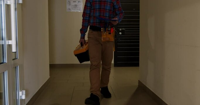 A mechanic with tools walks along the corridor of a building and holds a folder with a plan in front of him.