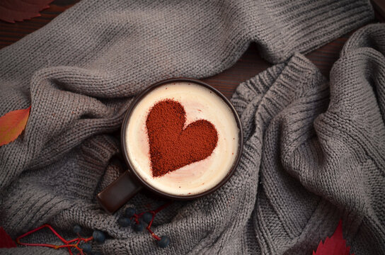 a cup of cappuccino with a stencil in the shape of a heart and a warm sweater flat lay