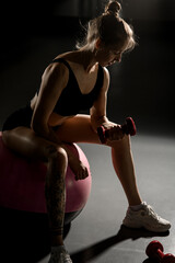 Side view of fit beautiful young woman exercising with dumbbells on fitness ball