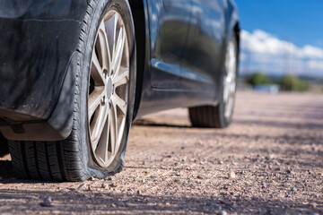 Flat tire on dirt road stranded in rural area blue sky black car