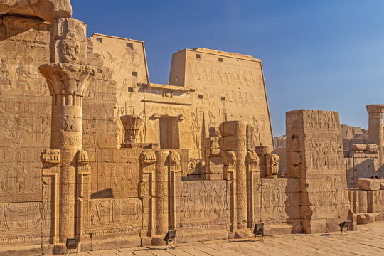 The ancient Egyptian temple of Horus in Edfu. Carved images of the gods are visible on the high wall. There are sculptures of birds at the entrance. 