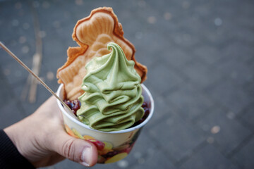 Hand hold a cup of matcha green tea soft ice-cream with Taiyaki, Japanese fish-shaped cake, and red...