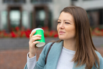 sleepy woman in coat with coffee to go in morning city outdoors. female drinking hot drink. lady holding beverage takeaway in spring, autumn on city street. concept wakefulness, have a nice day