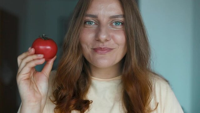 Smiling young woman showing tomato and lookin at camera, as she prepares dinner. Girl licks her lips. High quality FullHD footage