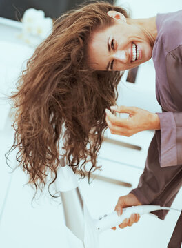Smiling young woman blow drying hair in bathroom