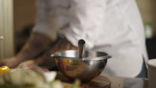 Close-up view of a professional male chef breaking an egg, putting it on a cooking bowl and mixing it in a professional kitchen