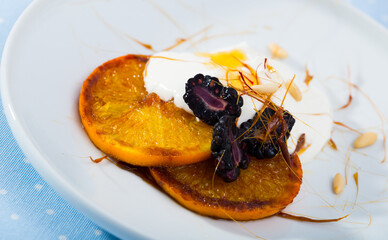 Sweet glazed orange slices with fresh dewberries and yogurt garnished with caramel and pine nuts