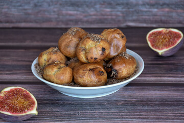 Delicious homemade profiteroles cakes with cocoa cream filling and chocolate chips. Choux pastry, cream puffs on plate, fig halves on wooden table background. 