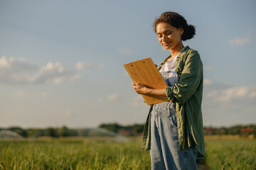 Female agronomist making notes on clipboard standing on field . Agricultural occupation concept