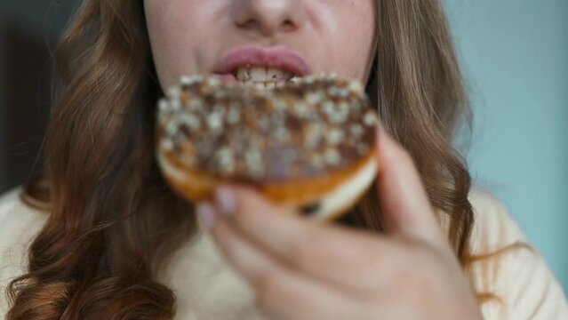 Close up portrait of a hungry 30s woman eating donut with white frosting. Girl sniffs sweet pastries. Eating donut when takeout and delivery. Fast food takeaway back home. High quality FullHD footage