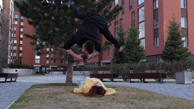 Caucasian woman lies on the grass. The man does a somersault over her and takes a photo. 