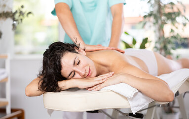 Obraz na płótnie Canvas Portrait of happy woman enjoying relaxing massage by professional masseur