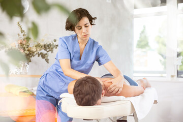 Adult woman masseuse massages back of young guy patient in office