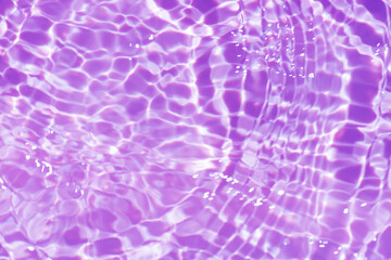Purple water with ripples on the surface. Defocus blurred transparent pink colored clear calm water surface texture with splashes and bubbles. Water waves with shining pattern texture background.