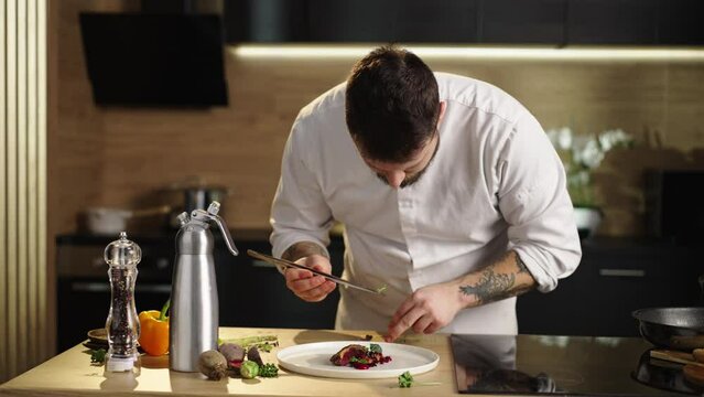 Slow-motion shot of a professional chef putting basil leaf on duck beetroot n the kitchen. Preparing dich for dinner