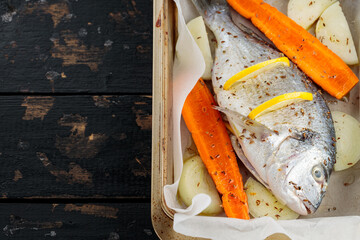 Raw dorado fish with lemon, vegetables and spices on parchment paper. Top view. Copy space