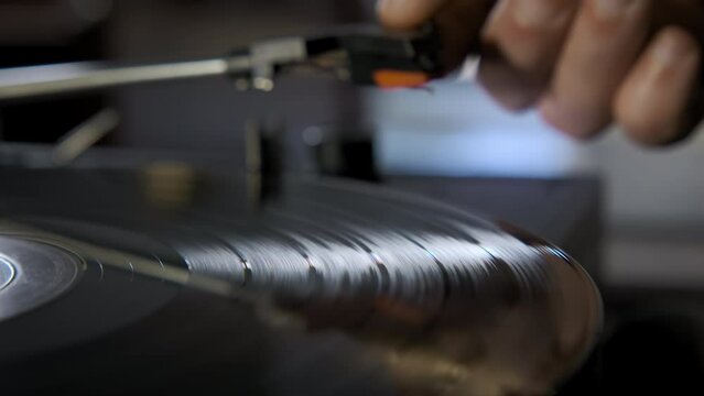 Close up shot of hands placing the vintage turntable on a spinning vinyl record. 