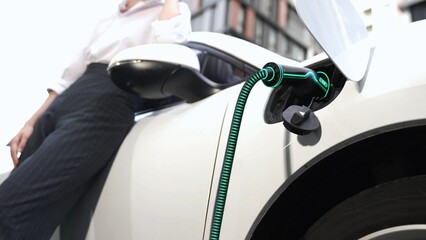 Businesswoman waiting after recharge electric car from charging station at city center or public...