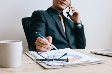 Successful mature Asian businessman talking on phone while checking document at the office