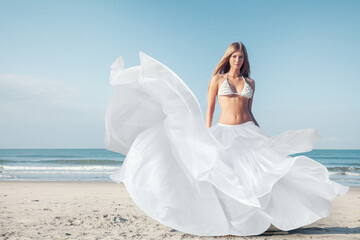 Beautiful woman in white fluttering dress in the wind against the background of the sea - obrazy, fototapety, plakaty