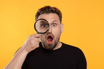Emotional man looking through magnifier on yellow background