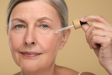 Senior woman applying cosmetic product on her aging skin against beige background. Rejuvenation...