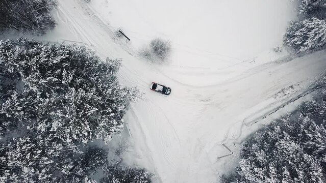 Black car automobile riding on snowy path at winter spruce forest nature scenery top drone shot. Aerial view modern auto vehicle transportation driving on snow road way peace fairy tale woodland 4k 3