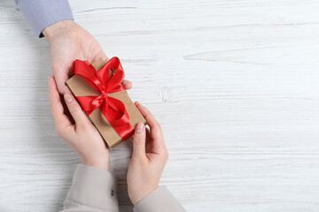 Man giving gift box to woman on white wooden table, top view. Space for text