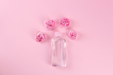 Bottle with baby oil and beautiful flowers on pink background, flat lay. Space for text