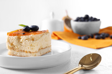 Piece of delicious cheesecake with blueberries and spoon on white table, closeup. Space for text