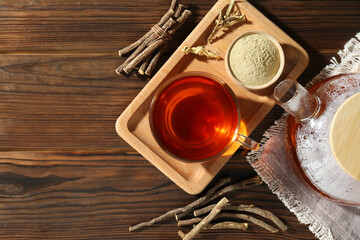 Aromatic licorice tea in cup, dried sticks of licorice root and powder on wooden table, flat lay. Space for text