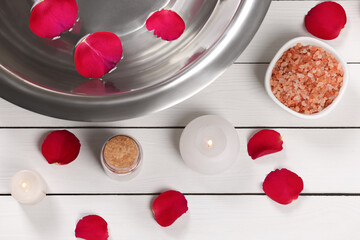 Flat lay composition with bowl of water and rose petals on white wooden table. Pedicure procedure