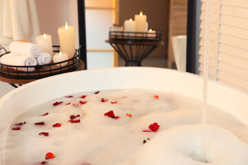 Bath tub with foam and rose petals in bathroom