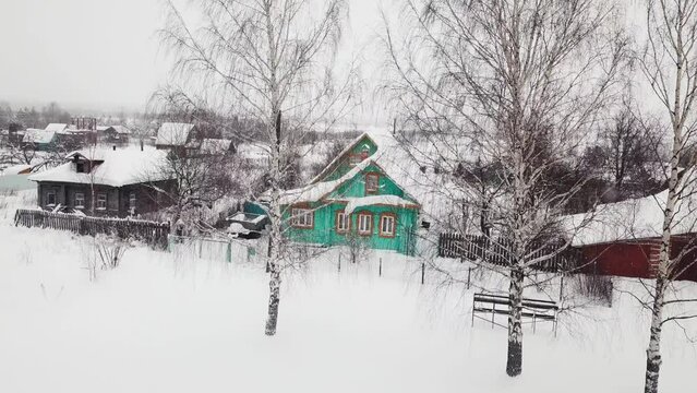 Flying to wooden old turquoise house in village in snowfall snowstorm cold frozen weather. Aerial view of rural suburban area, country lifestyle, countryside countrified hamlet hillbilly concept 4k 3