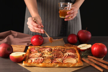 Woman adding honey to freshly baked apple pie at table, closeup
