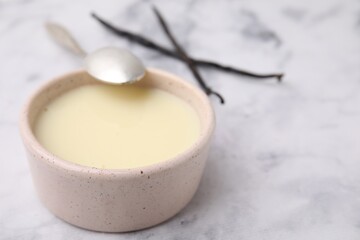 Bowl with condensed milk, vanilla pods and spoon on white marble table, closeup. Space for text