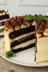 Delicious tiramisu cake with cocoa powder and mint leaves on wooden table, closeup
