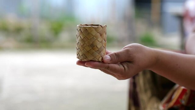 An Indonesian woman hand taking terasi or shrimp paste in ecopacking. Indonesian seasoning made from fermented shrimp or fish in ecopackaging from bag weaving from mangrove palm leaves.
