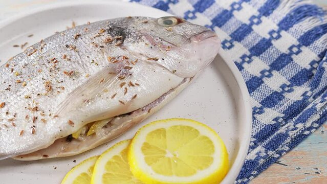 Raw dorado fish with lemon and sprinkled with cumin on white plate. Handheld shot