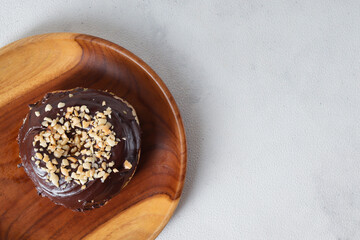 Flat lay top view of delicious sweet chocolate glazed donut with cashew nut served on wooden plate. Isolated image on white background