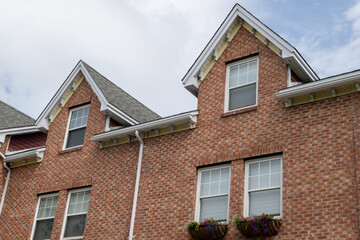 A row of brown brick townhouses with peaked gable roofs, and double hung windows with white trim....
