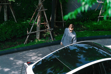 Young man travel with EV electric car charging in green sustainable city outdoor garden in summer...